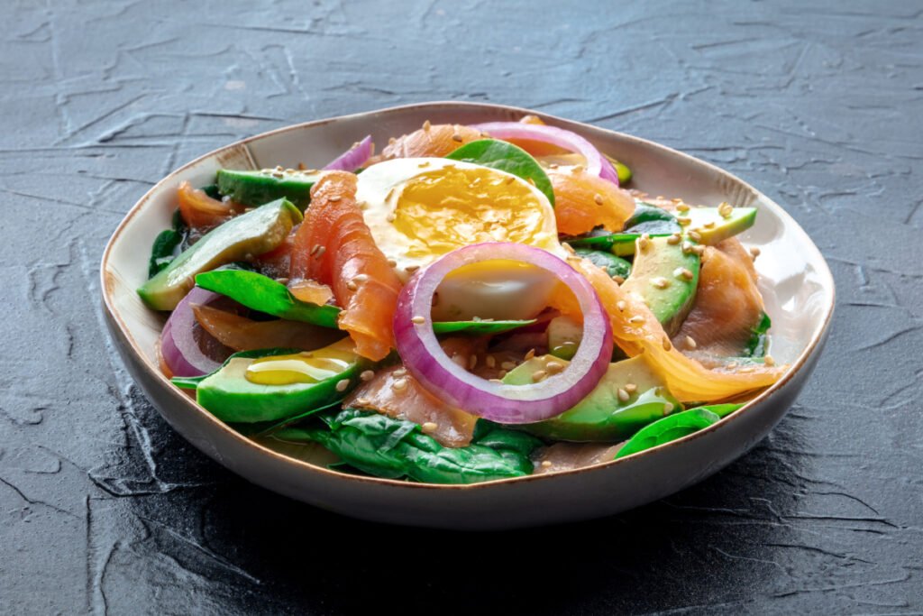 Healthy bowl of salmon, egg, avocado, olive oil, onion, and sesame seeds