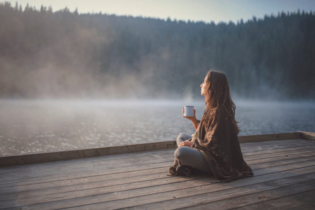 Woman with mug in her hand watching morning fog over a lake