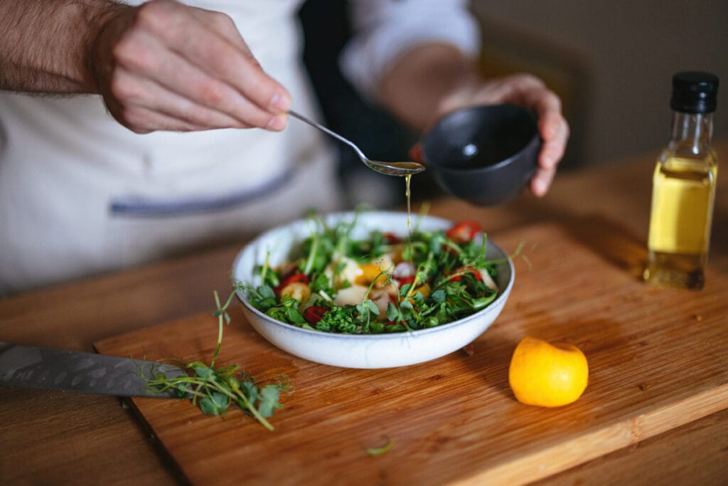 Faceless man adding olive oil to a healthy mixed green salad